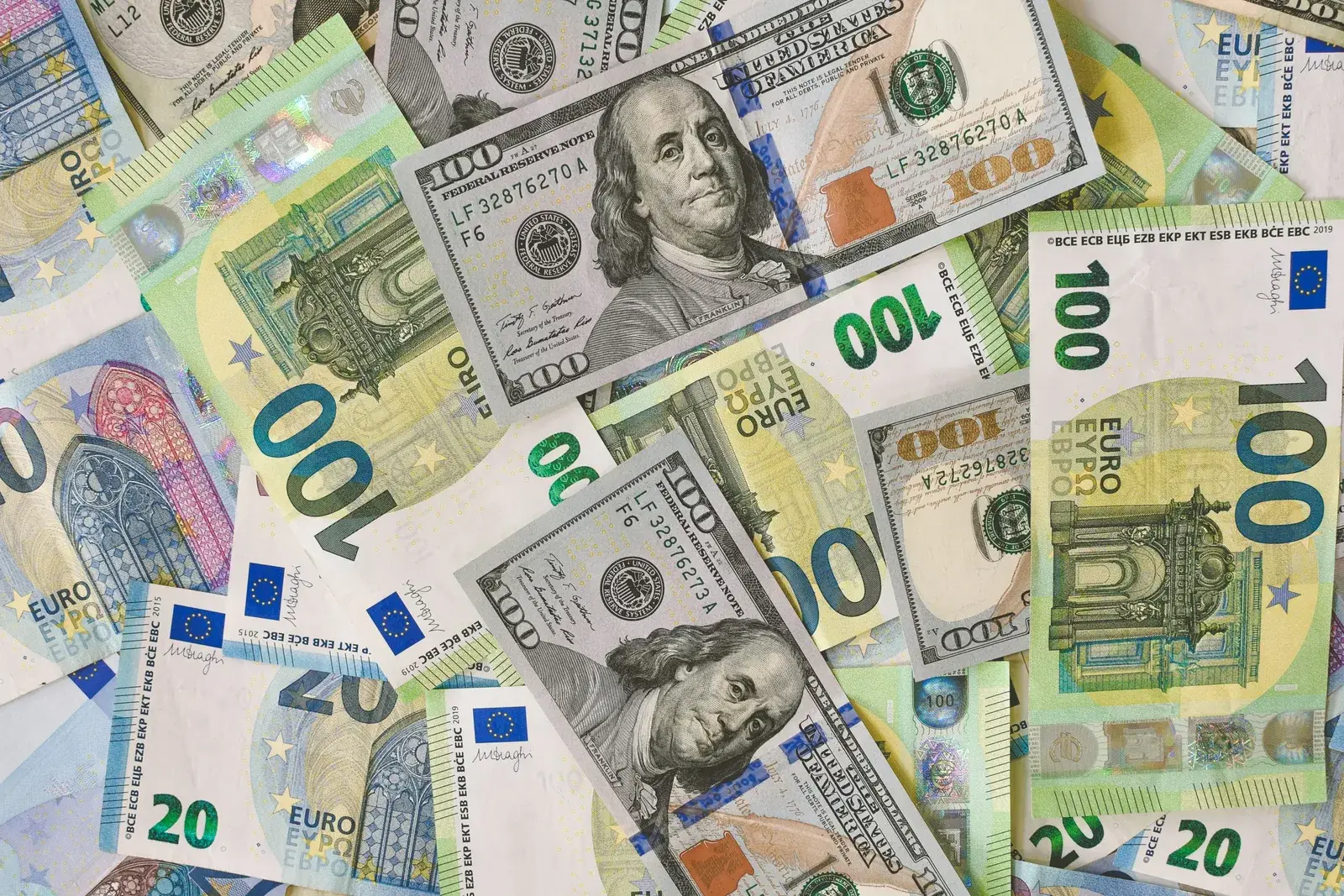 Billetes de 100 dólares y de 100 y 20 euros desparramados cubriendo toda la superficie