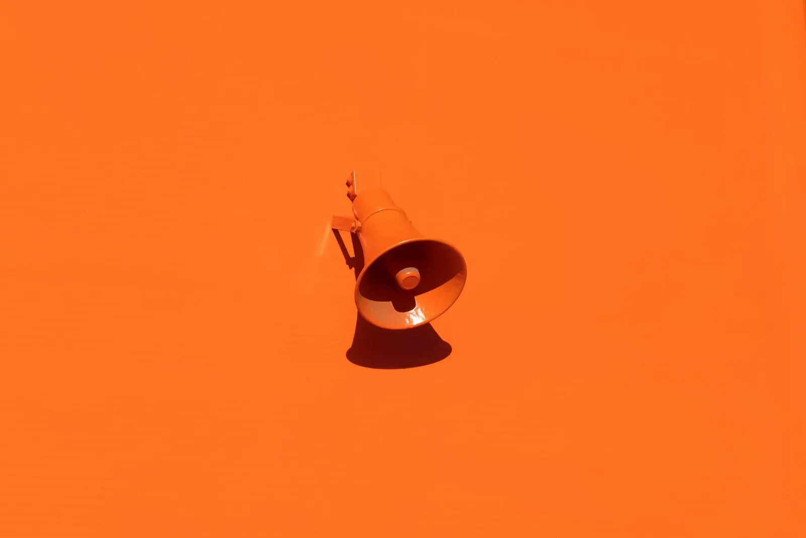 Megáfono naranja montado sobre una pared del mismo color naranja