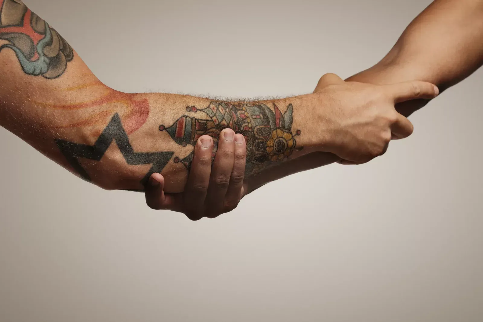 Dos brazos, uno tatuado, que se sostienen con firmeza por el antebrazo sobre fondo neutro