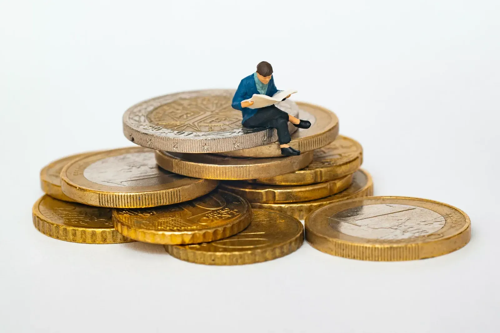 Figura en miniatura leyendo un diario sentada sobre una pila de monedas de euro