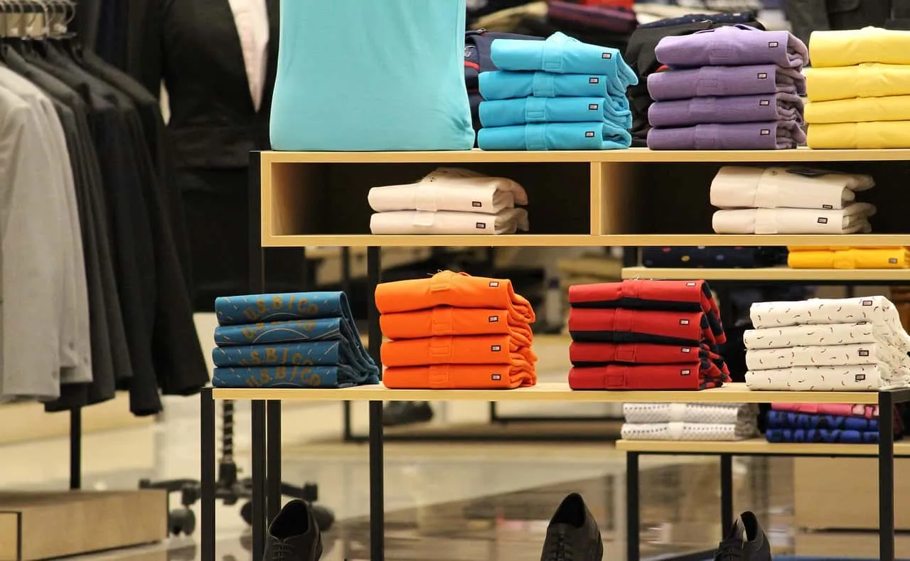Remeras y camisas dobladas por color en los estantes de una tienda de ropa