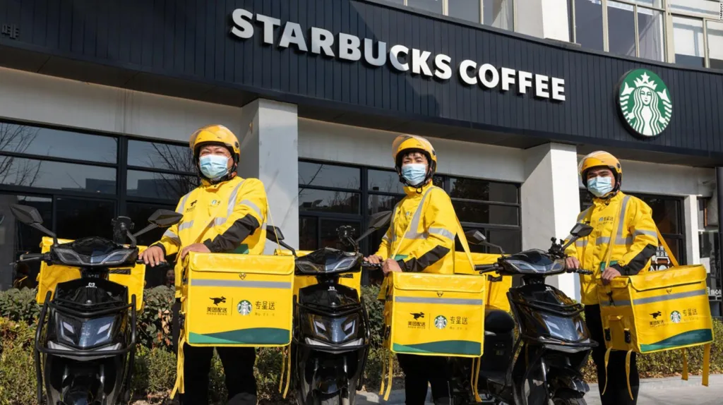 Tres repartidores con uniforme amarillo y scooters eléctricos frente a un local de Starbucks Coffee